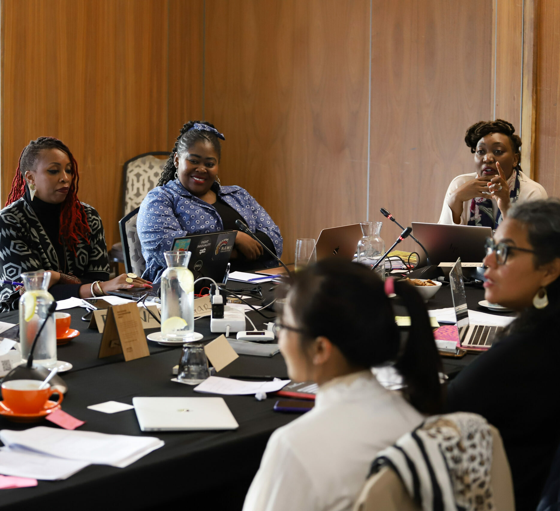 Black and brown women in discussion, sitting around an office table.